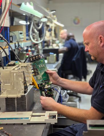 Engineer working on variable speed drive repair at Neutronic Technologies workshop, testing and servicing an industrial drive unit on a workbench.