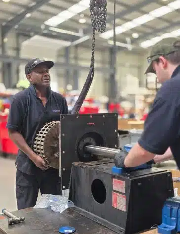 Engineers performing industrial fans repair at Neutronic Technologies workshop, working on a large industrial fan assembly with a shaft and lifting chain for maintenance.