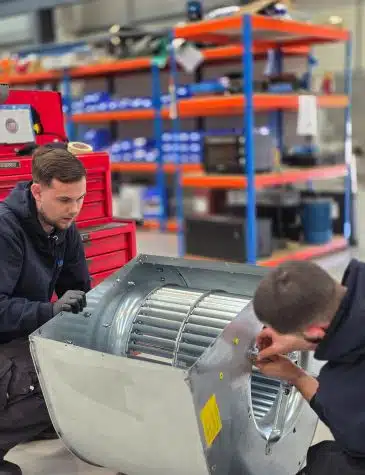 Engineers carrying out fan repair at Neutronic Technologies workshop, inspecting and adjusting a industrial fan housing with an impeller on a workbench.