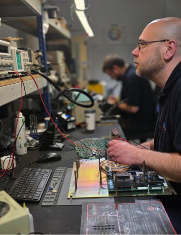 Close-up of industrial controller repairs showing precision testing of electronic components on an industrial control board by an experienced technician.