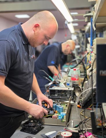 An engineer is performing power supply repairs at an electronics workbench, inspecting and testing internal components.