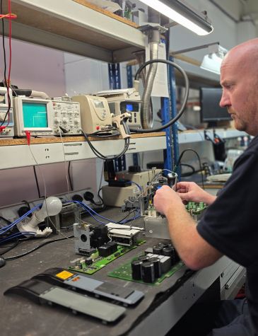 An engineer is performing power supply repairs on electronic components using diagnostic test equipment at a specialised workbench.